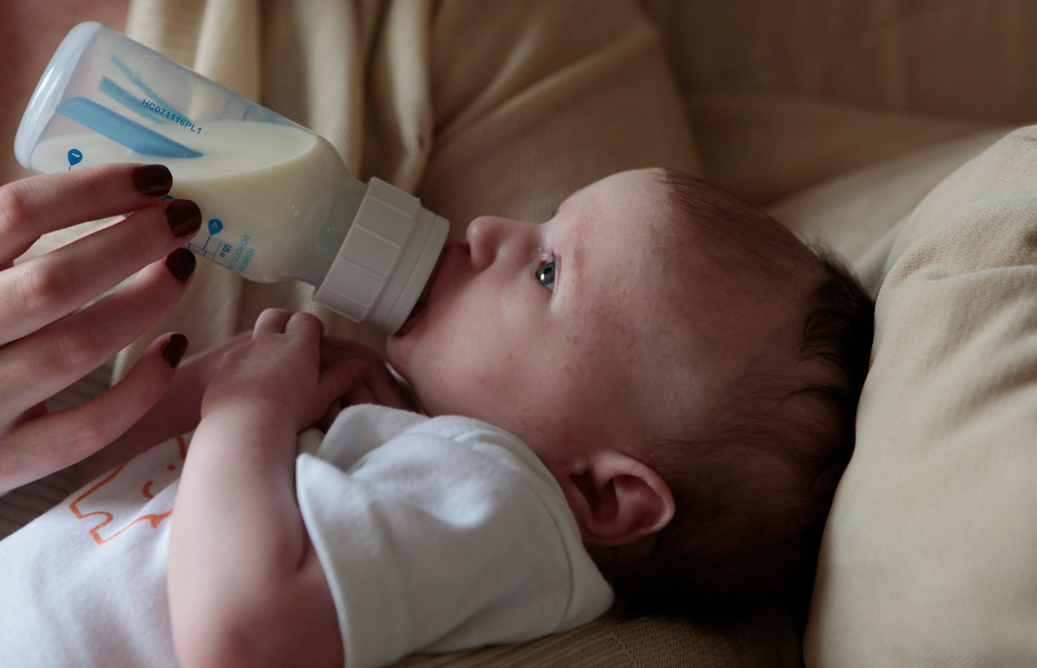 Baby drinking from a bottle held by an adult
